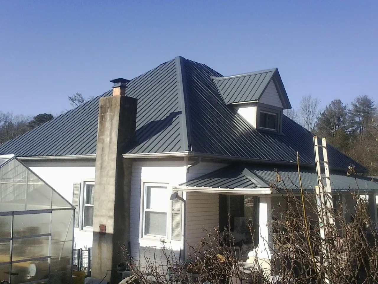 Dark blue standing seam metal roof on a white farmhouse with dormer — Slate & Tile Roof Repair by Roofing Brothers in Advance