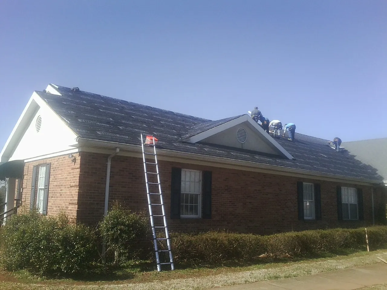 Crew tearing shingles off a brick ranch roof with a ladder set — Emergency Roof Repair work by our crew in Advance