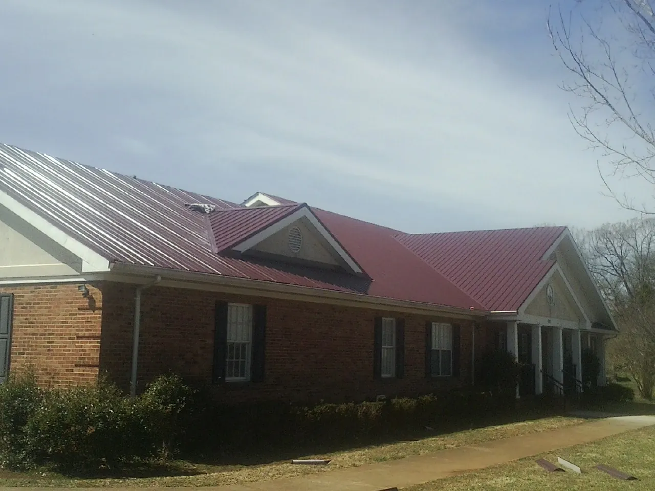 Red metal roof with gabled entries on a long brick building, from a Hail Damage Roof Repair job in Advance