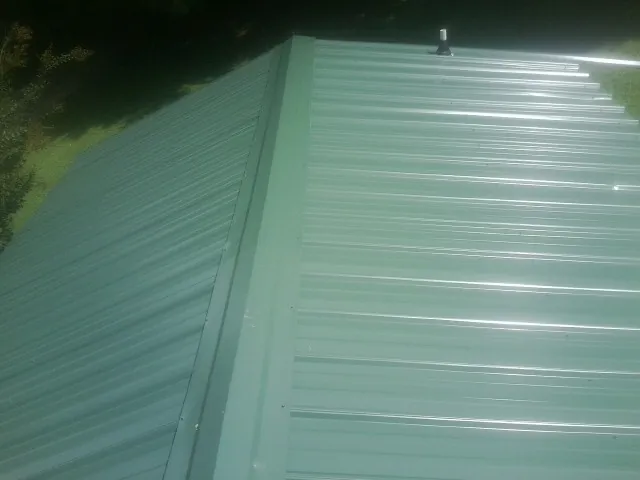 New green metal panels meeting at the ridge of a roof — Flat Roof Repair work by our crew in Advance