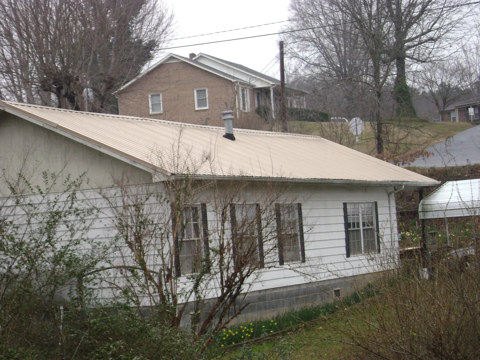 Tan metal roof on a white sided house set into a hillside — Commercial Roofing by Roofing Brothers in Advance