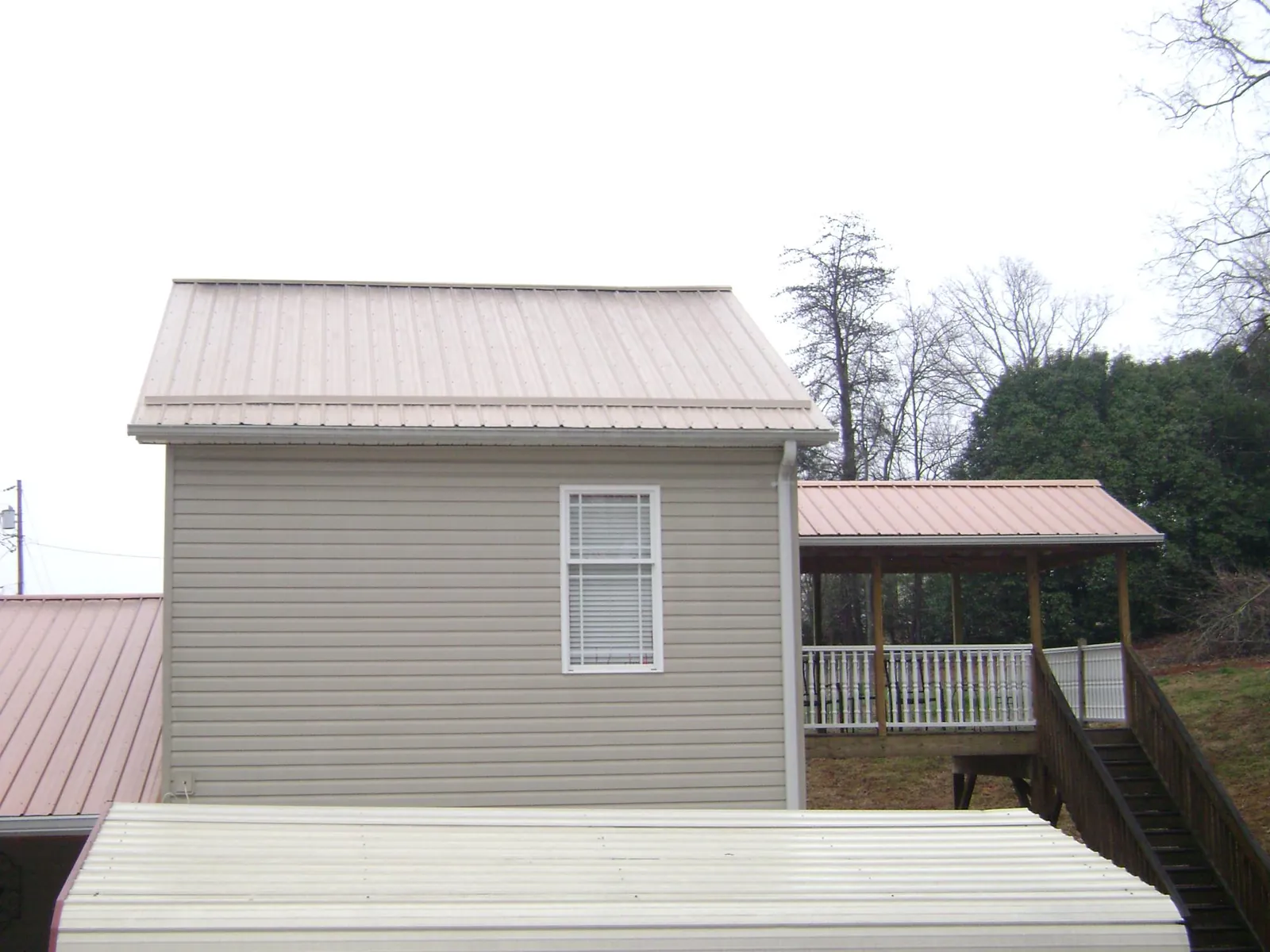 Tan metal roofs on a two story addition and attached porch, from a Roof Replacement job in Advance